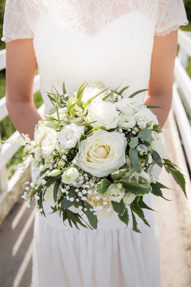 A radiant bride holding a custom bridal bouquet of roses and greenery, designed by Dorothy Marchant Florists for a magical wedding in Bexhill-on-Sea.
